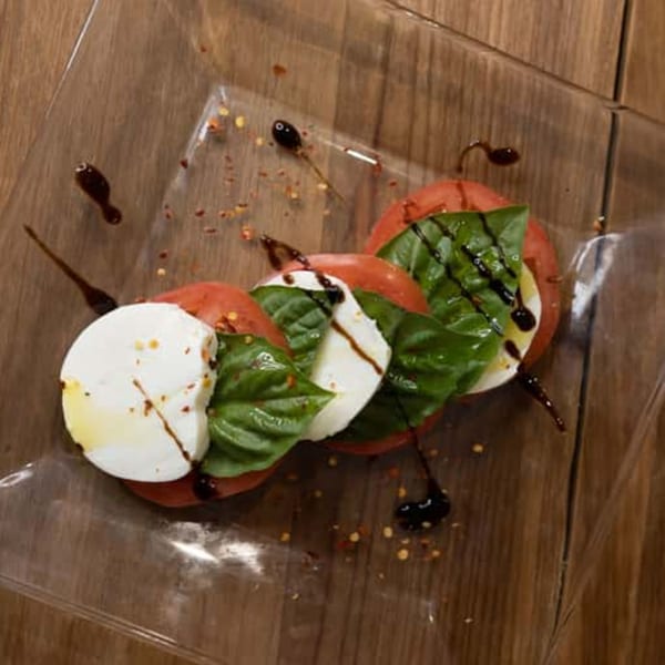Caprese salad with sliced tomatoes, fresh mozzarella, basil, and balsamic glaze on a clear plate.