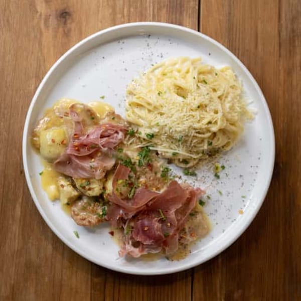 Andiamo Italian Grill's chicken and pasta dish, topped with prosciutto, cheese, and herbs on a white plate.