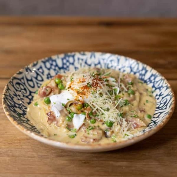 Creamy Italian pasta with mushrooms, peas, parmesan, and paprika in a decorative bowl on wood.