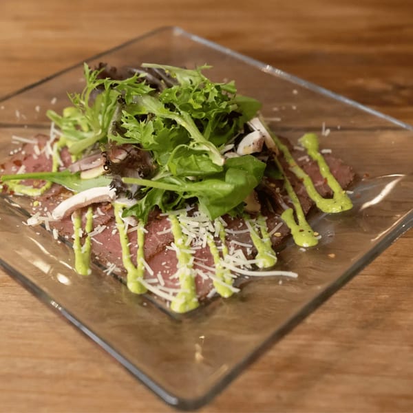 Andiamo Italian Grill's carpaccio with arugula, mushrooms, parmesan, and green sauce on a glass plate.