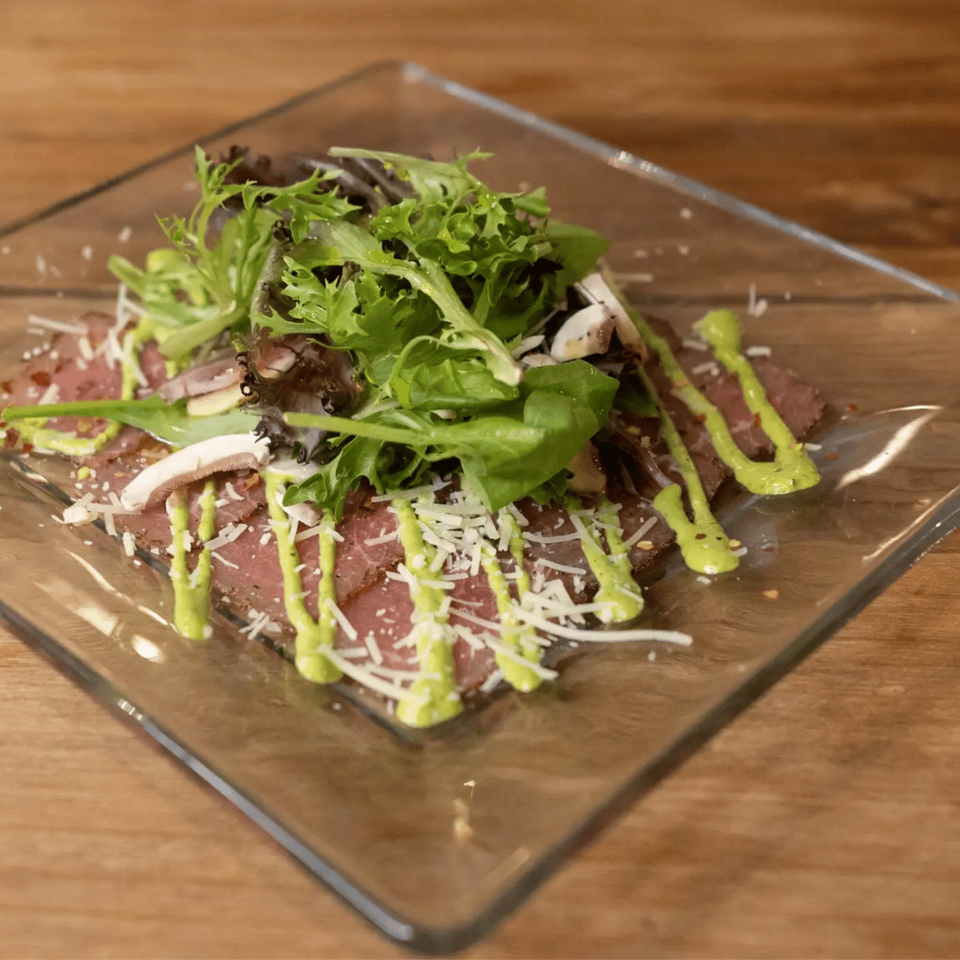 Andiamo Italian Grill's carpaccio with arugula, mushrooms, parmesan, and green sauce on a glass plate.
