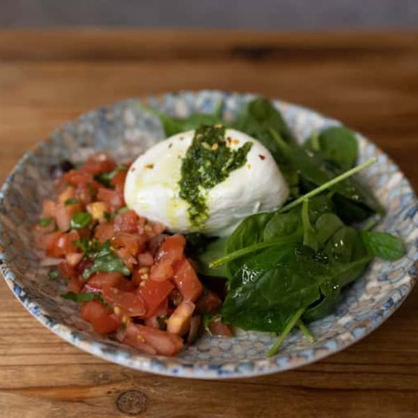 Andiamo Italian Grill's burrata with diced tomatoes, fresh spinach, and pesto on a patterned plate.