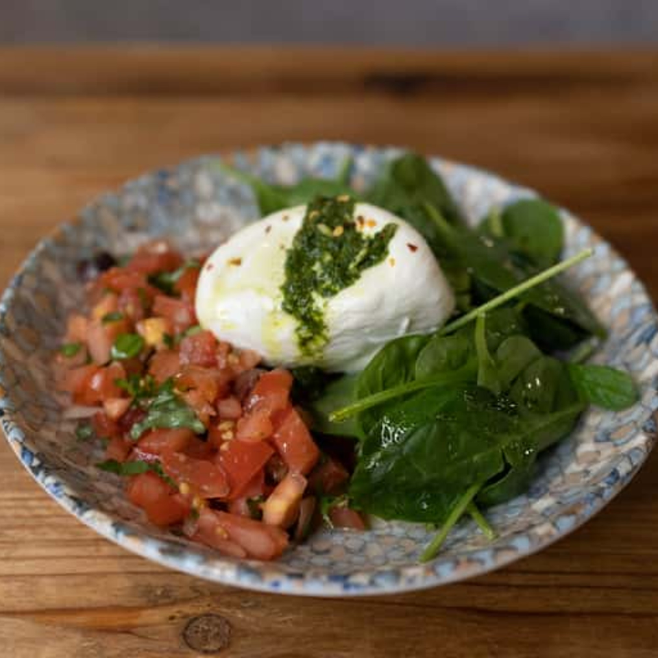 Andiamo Italian Grill's burrata with diced tomatoes, fresh spinach, and pesto on a patterned plate.