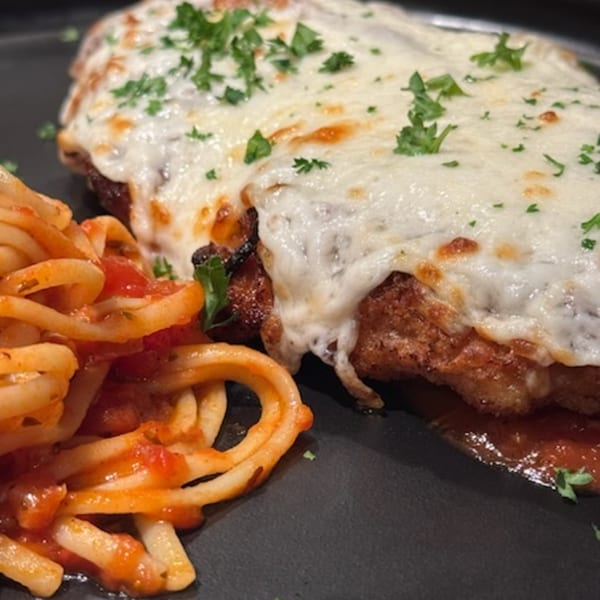 Chicken Parmesan with melted mozzarella cheese and parsley, served alongside spaghetti with red sauce.
