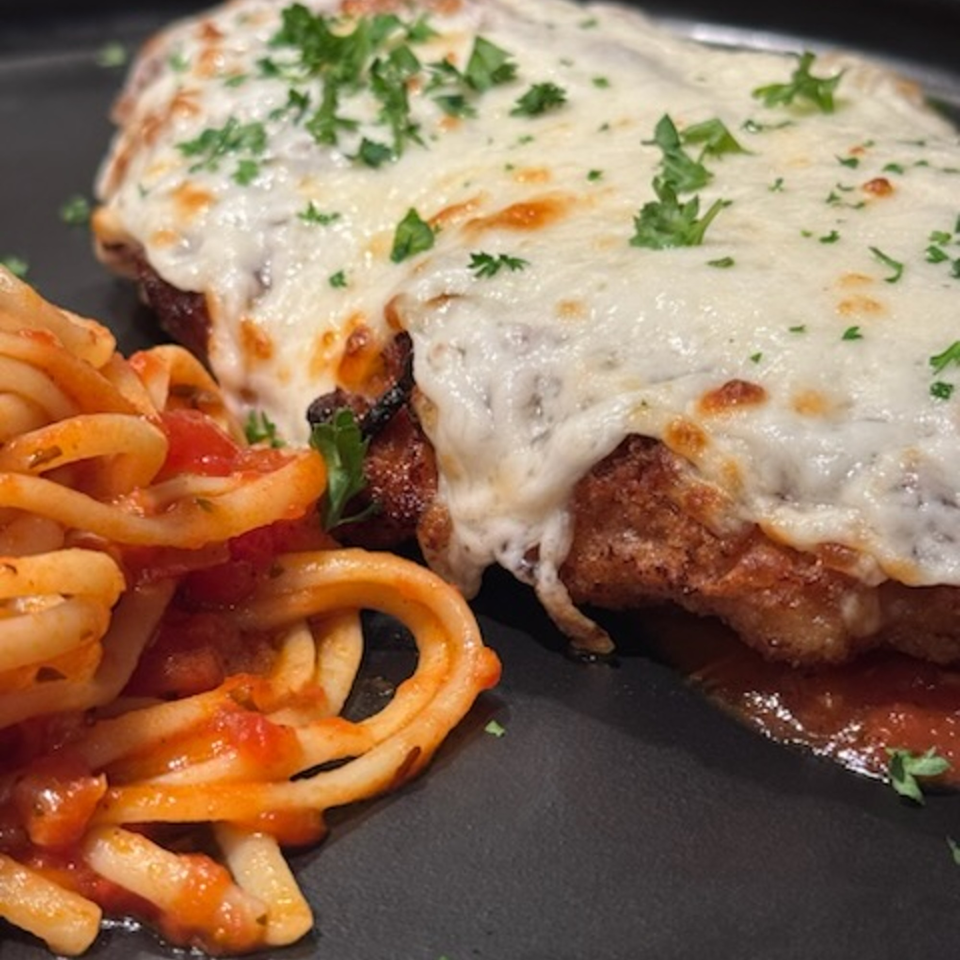 Chicken Parmesan with melted mozzarella cheese and parsley, served alongside spaghetti with red sauce.