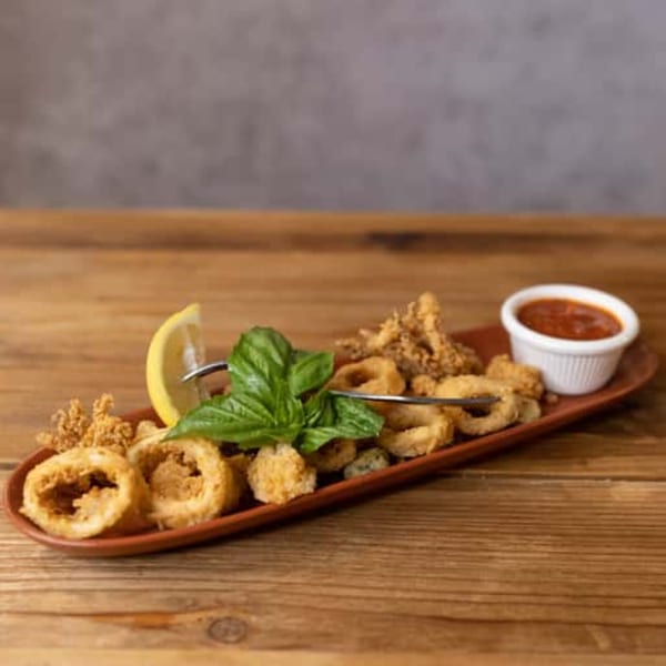 Crispy fried calamari rings and tentacles with a lemon wedge, fresh basil, and marinara sauce.