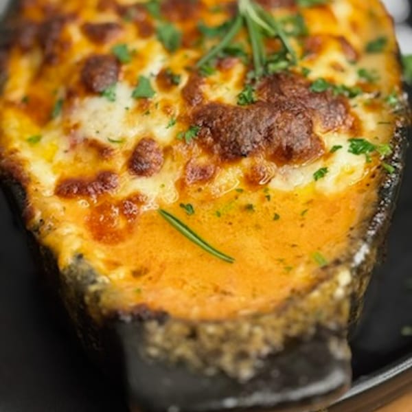 Close-up of a baked Italian dish with melted cheese, a rich orange sauce, and fresh herbs.