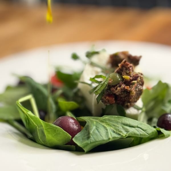 Olive oil drizzling over an Italian salad with spinach, grapes, and feta cheese.