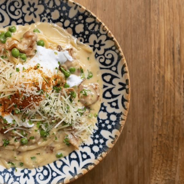 Creamy Italian pasta with chicken, peas, parmesan, and paprika in a decorative bowl on wood.