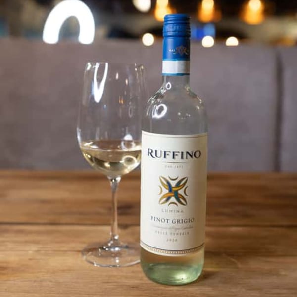 A bottle of Ruffino Lumina Pinot Grigio and a glass of white wine on a wooden table.