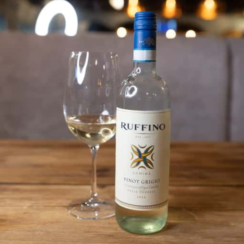 A bottle of Ruffino Lumina Pinot Grigio and a glass of white wine on a wooden table.