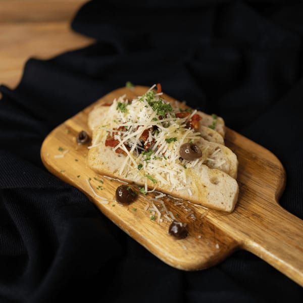 Italian bruschetta with shredded cheese, sun-dried tomatoes, parsley, and olives on a wooden board.
